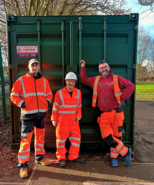 3 people in orange high visibility clothing stood in front of a green 10ft storage container